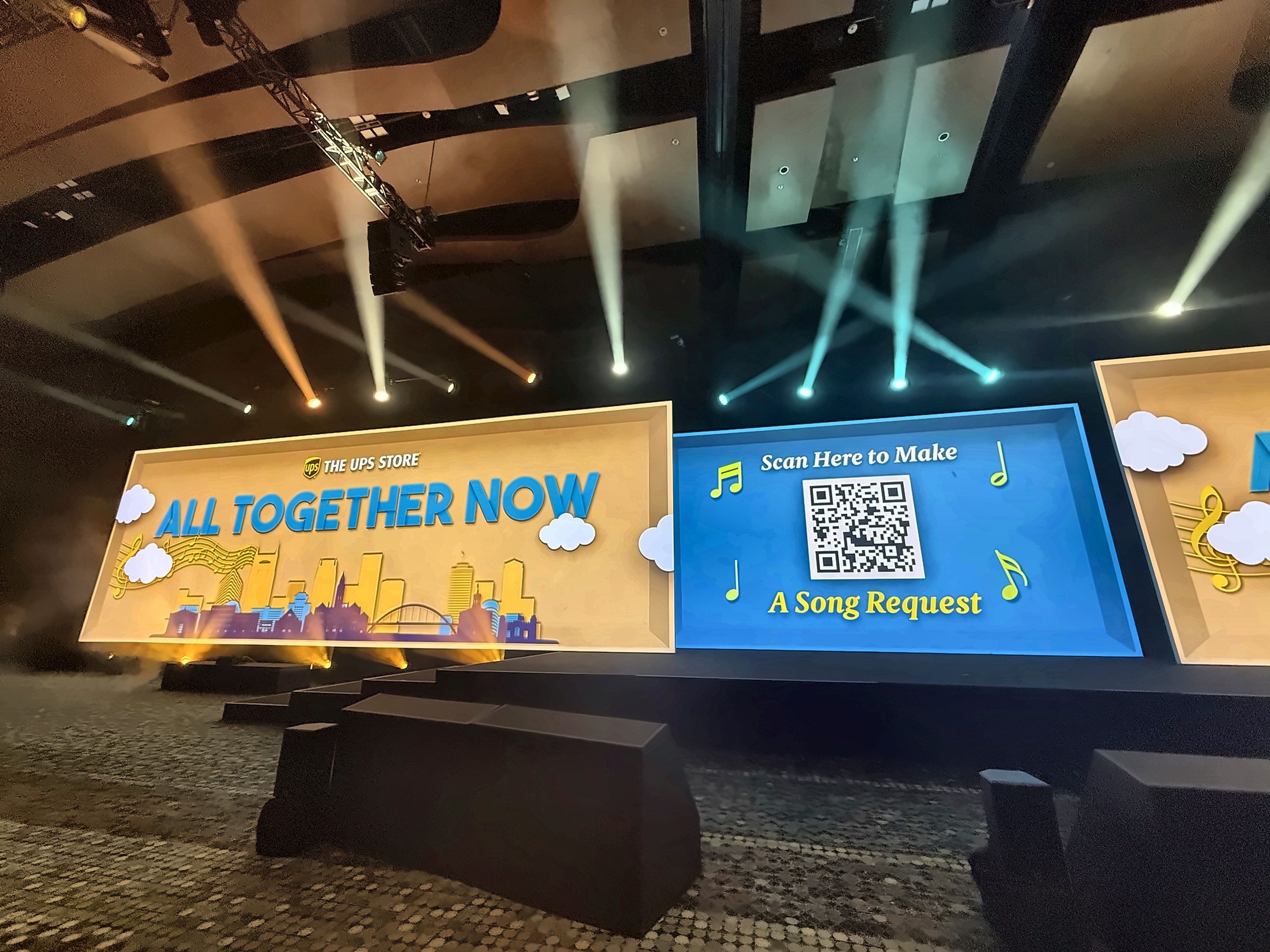 Live photo of the All Together Now day-theme screens and song-request kiosk on the general session stage